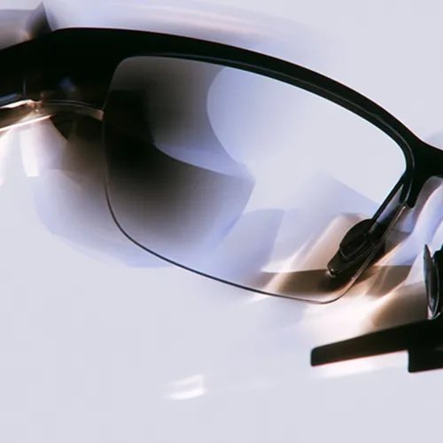 Close-up of black-framed eyeglasses with reflections on the lens against a light background.