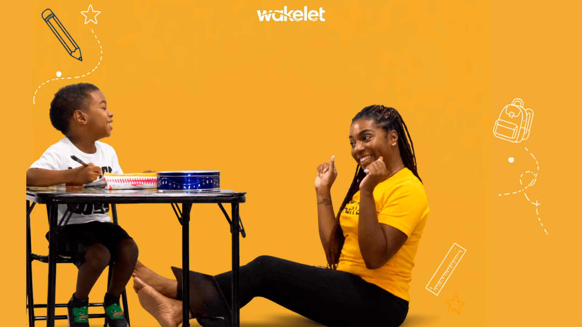 An image of a young boy sat down on a desk interacting with his teacher