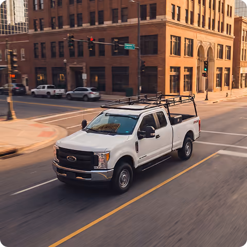 White pickup truck with a roof rack driving on a city street
