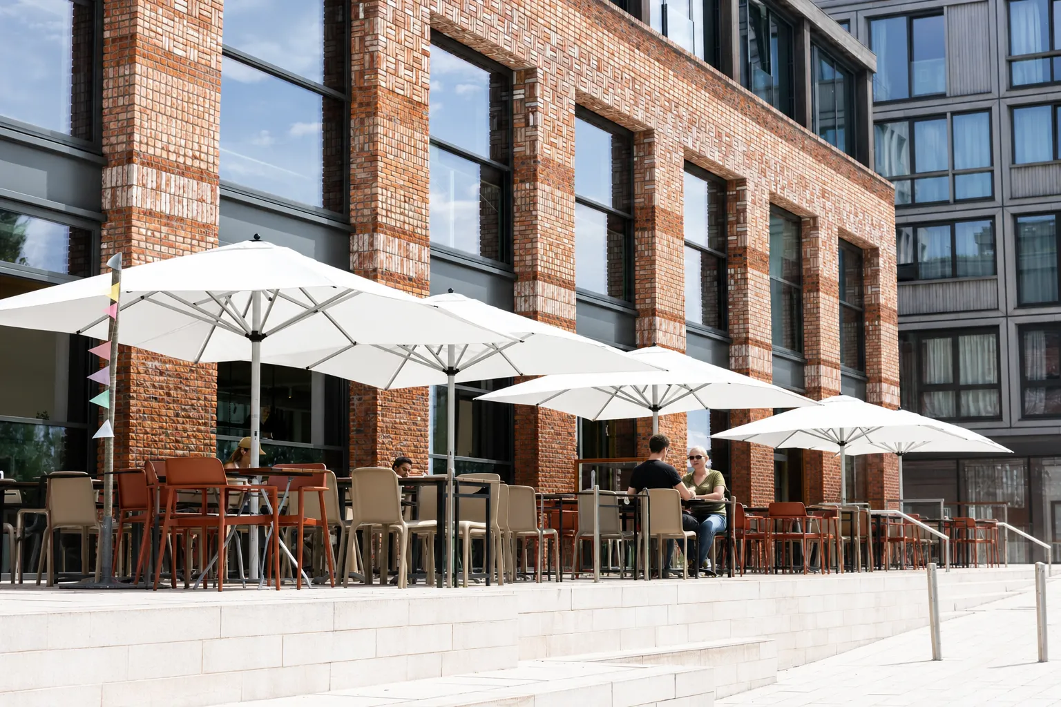Terras van Papillon zonder beplanting, met alleen tafels, stoelen en witte parasols