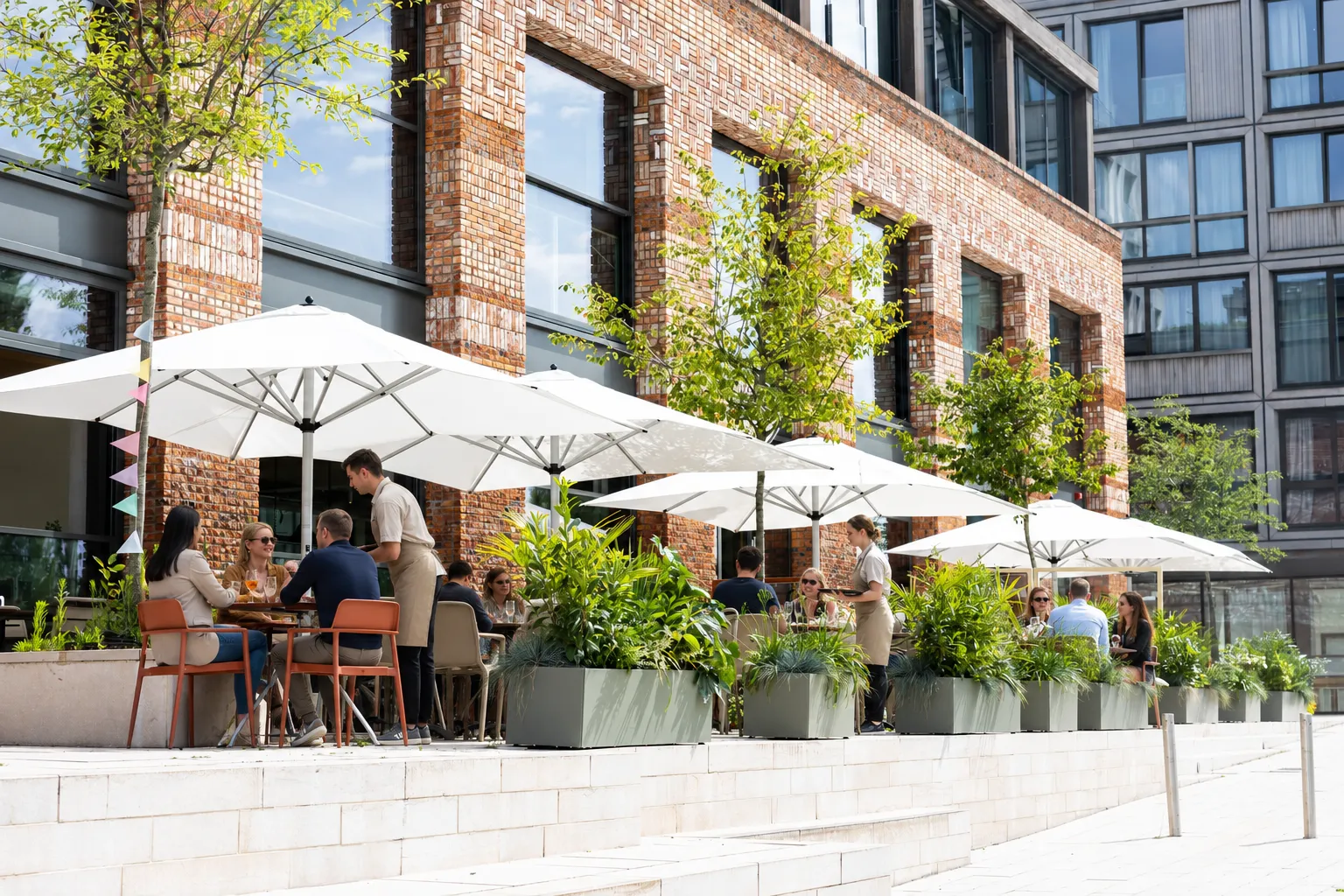 Terras van Papillon na de inrichting met grijze plantenbakken, jonge bomen en parasols