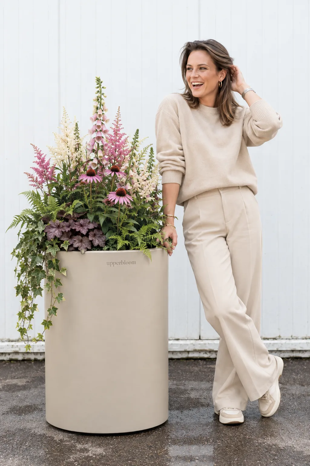 Vrouw naast een hoge zandkleurige plantenbak met vingerhoedskruid, zonnehoed en astilbe