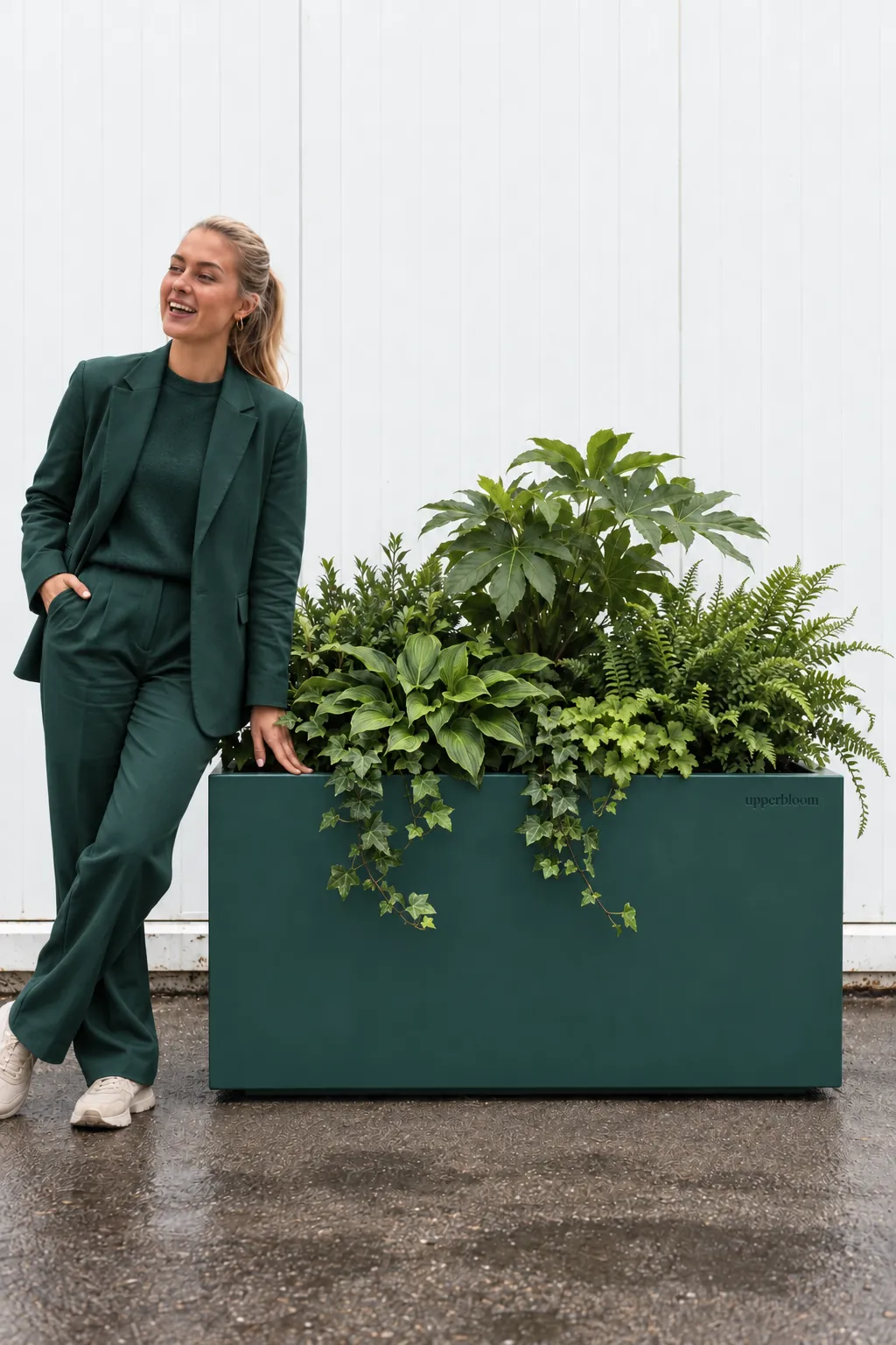 Vrouw leunt tegen een donkergroene plantenbak met vingerplant, hosta, varens en klimop