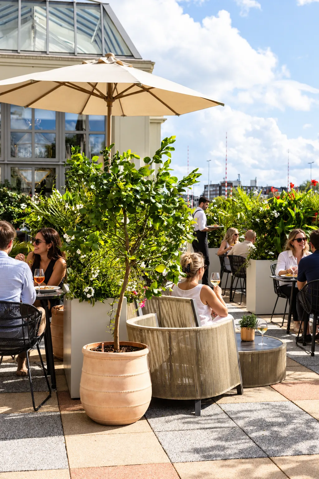 Terracotta pot met boompje en lichte plantenbakken met witte bloeiers op het terras van het Amstel Hotel