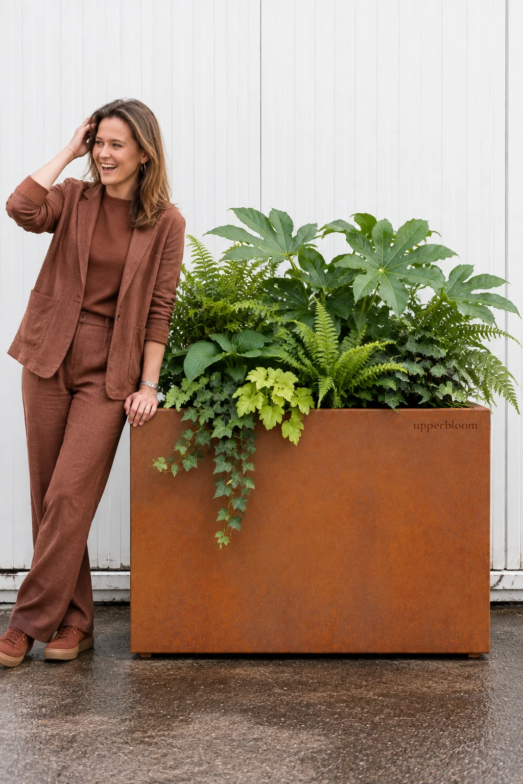 Vrouw naast een brede cortenstalen plantenbak met vingerplant, varens, heuchera en klimop