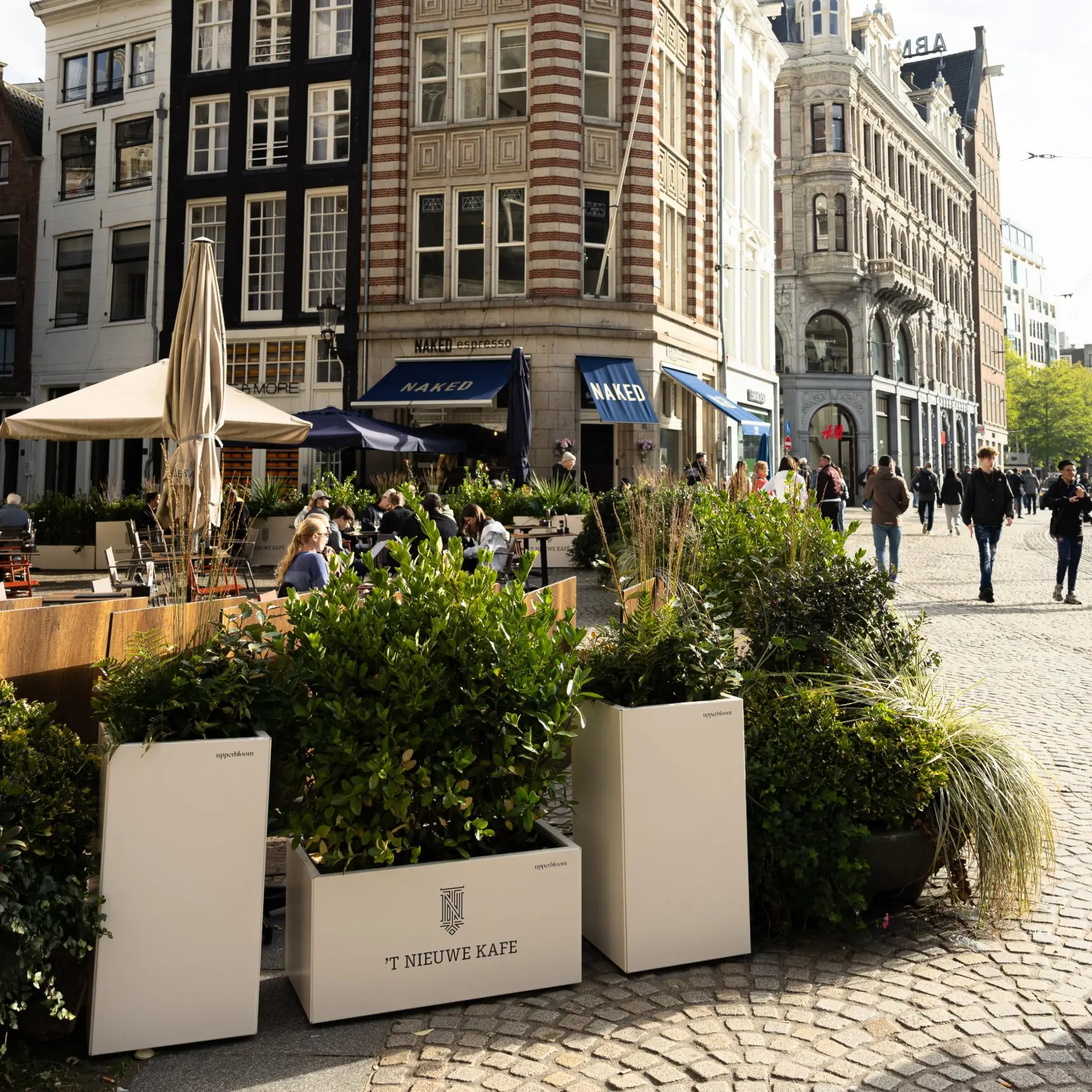 Witte plantenbakken met heesters en siergras rond het terras van 't Nieuwe Kafé op de Dam