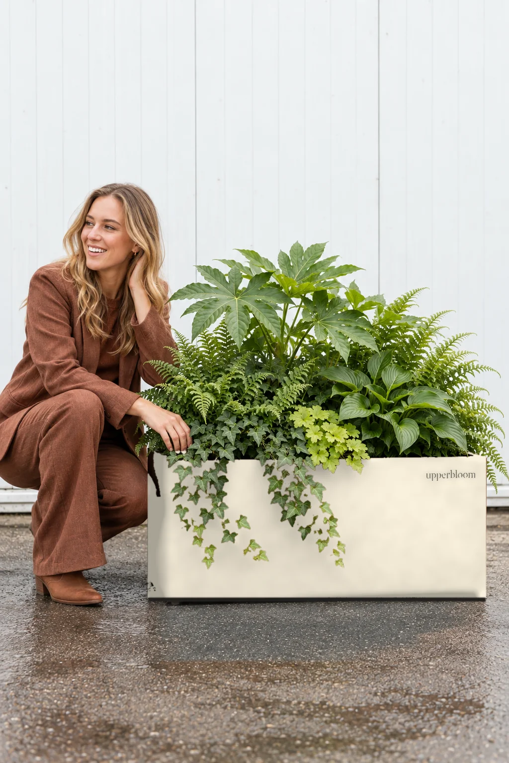 Vrouw gehurkt naast een crèmekleurige plantenbak met vingerplant, hosta, varens en klimop
