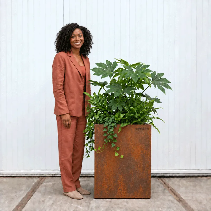 Vrouw naast een hoge cortenstalen plantenbak met vingerplant, varens en klimop