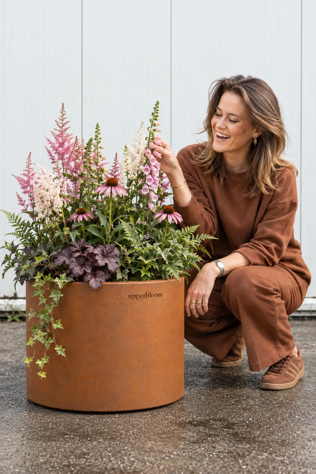 Vrouw hurkt bij ronde cortenstalen plantenbak met astilbe, vingerhoedskruid en echinacea