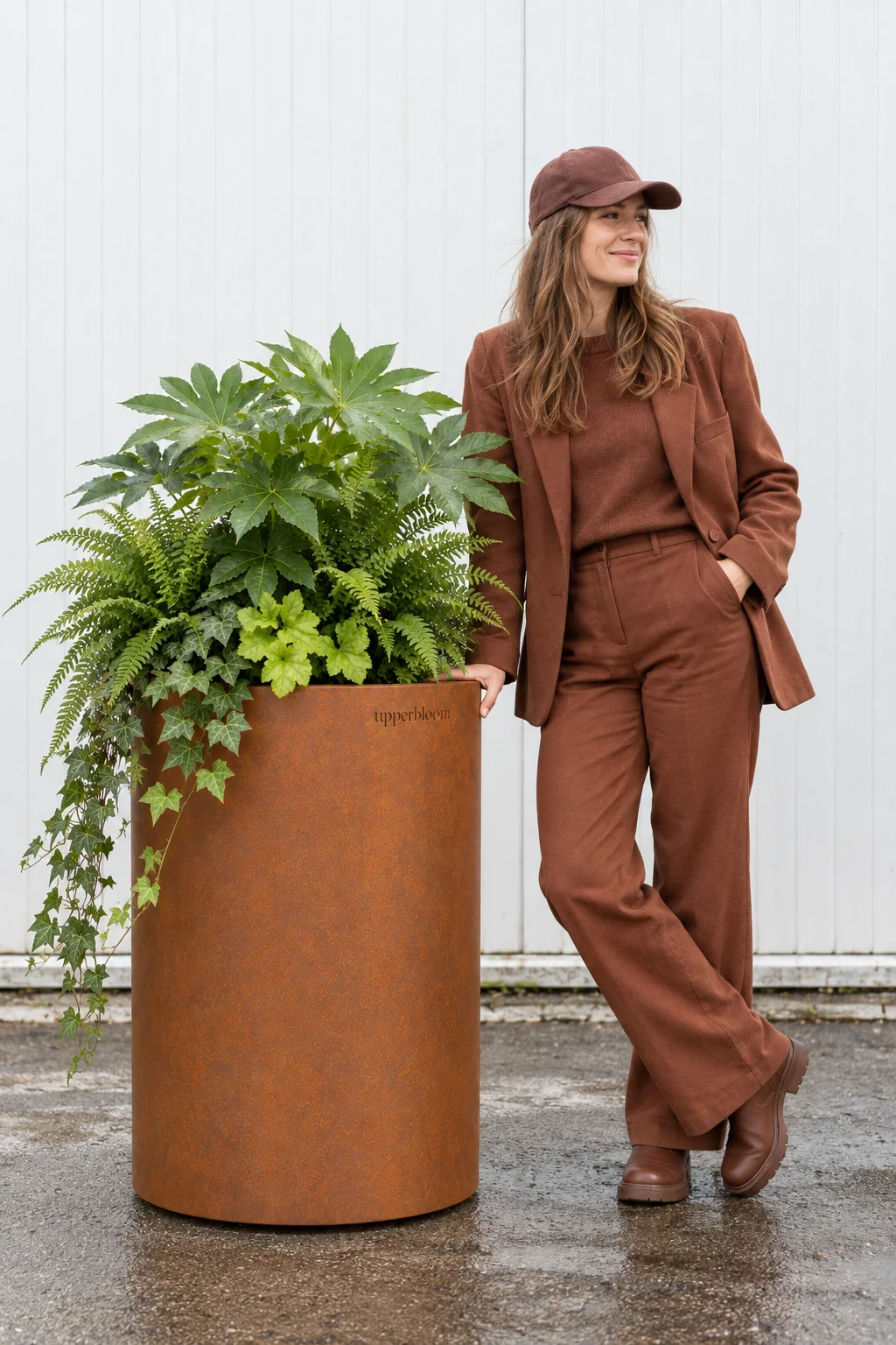 Vrouw naast hoge ronde cortenstalen plantenbak met vingerplant, varens en hangende klimop