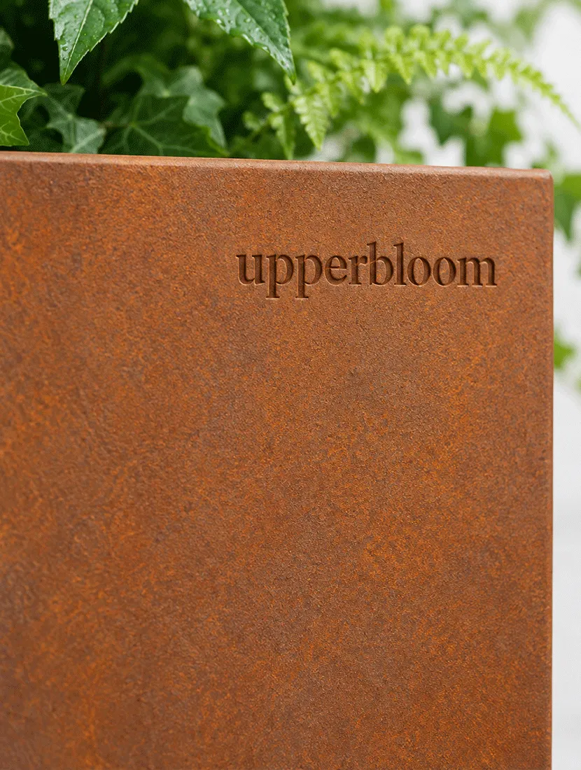 Detail van cortenstalen plantenbak met ingeslagen logo onder varens en klimop