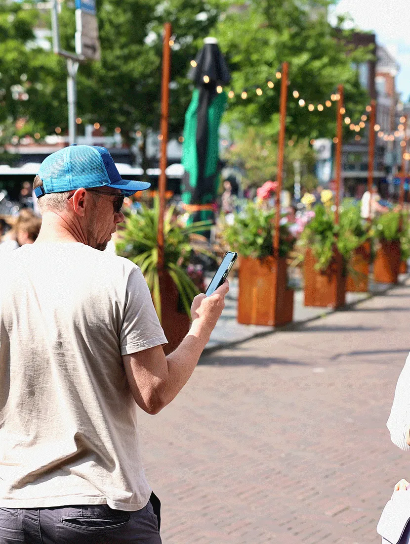 Voorbijganger op de Neude met een rij cortenstalen plantenbakken en prikverlichting op de achtergrond