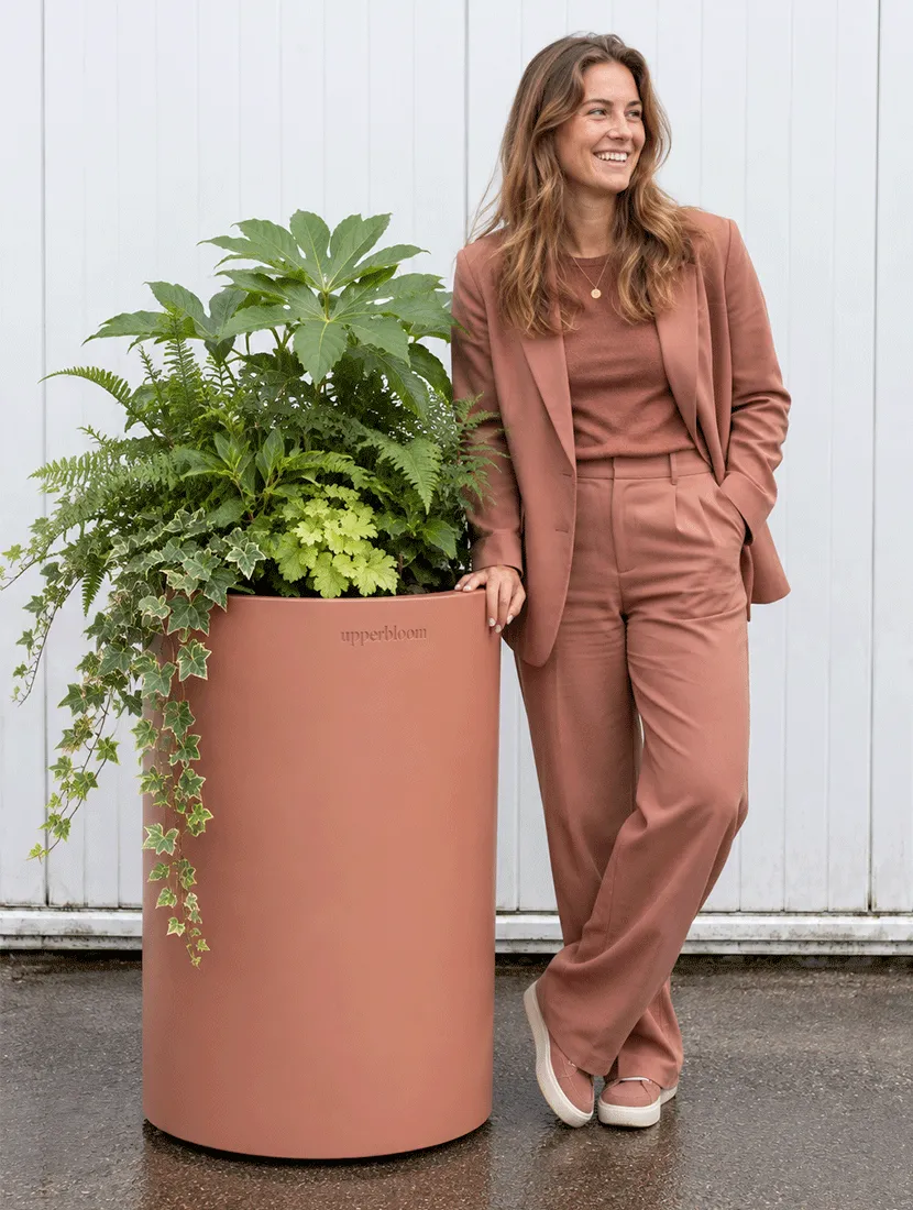 Vrouw naast hoge terracotta ronde plantenbak met vingerplant, varens en hangende klimop