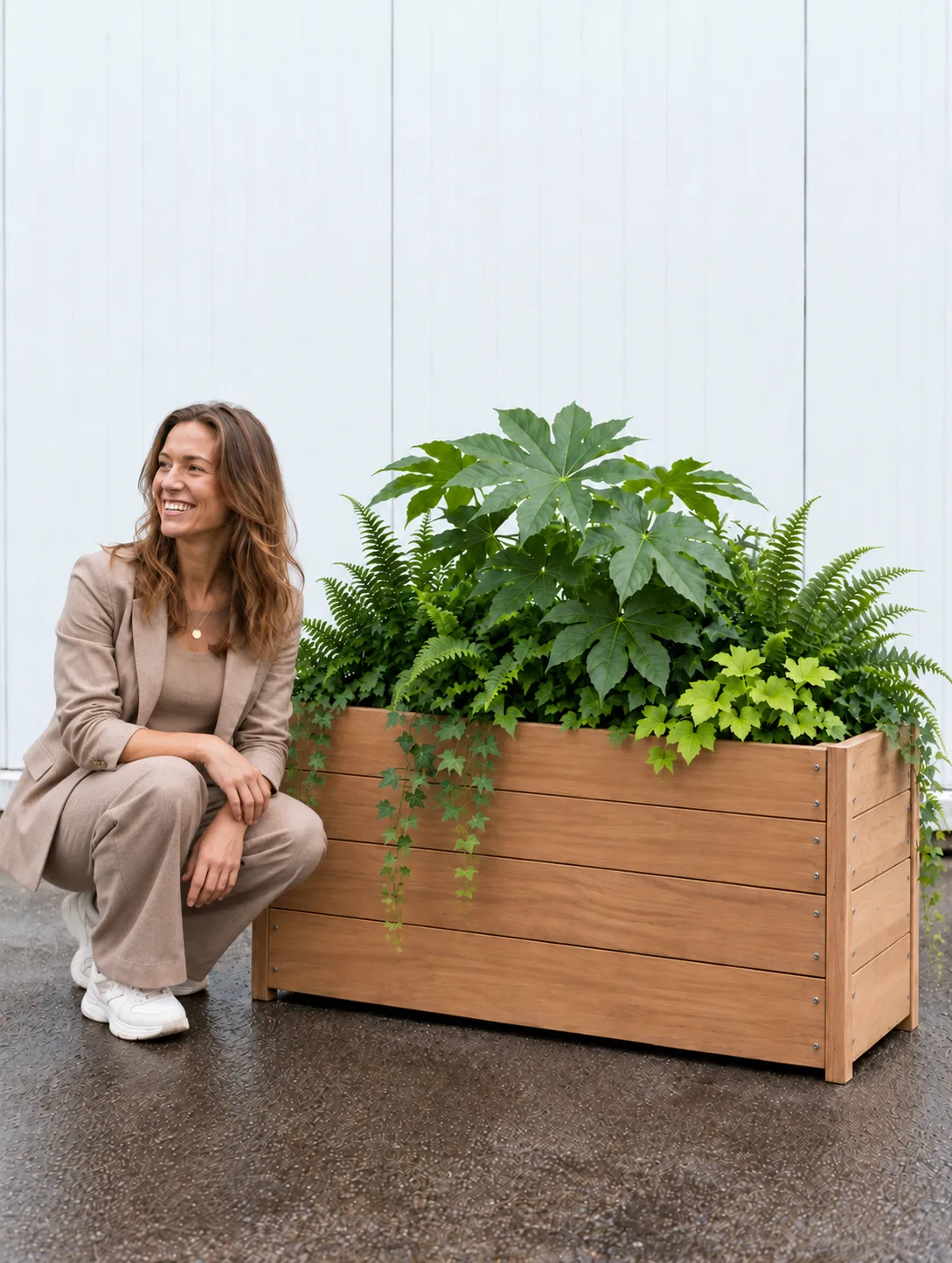 Vrouw hurkt naast houten plantenbak met vingerplant, varens en hangende klimop