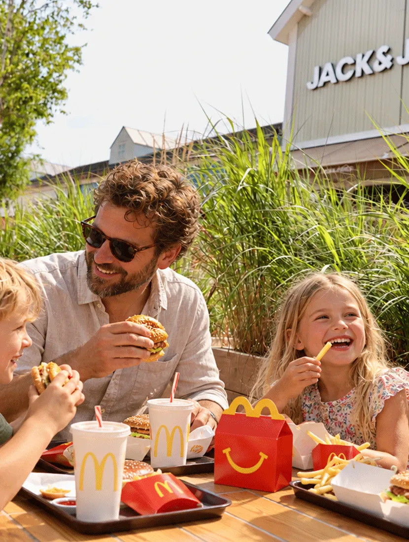 Vader en twee kinderen eten op het terras, met hoge siergrassen in de plantenbakken achter hen