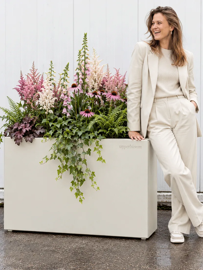 Vrouw bij lichte rechthoekige plantenbak met astilbe, echinacea, varens en hangende klimop