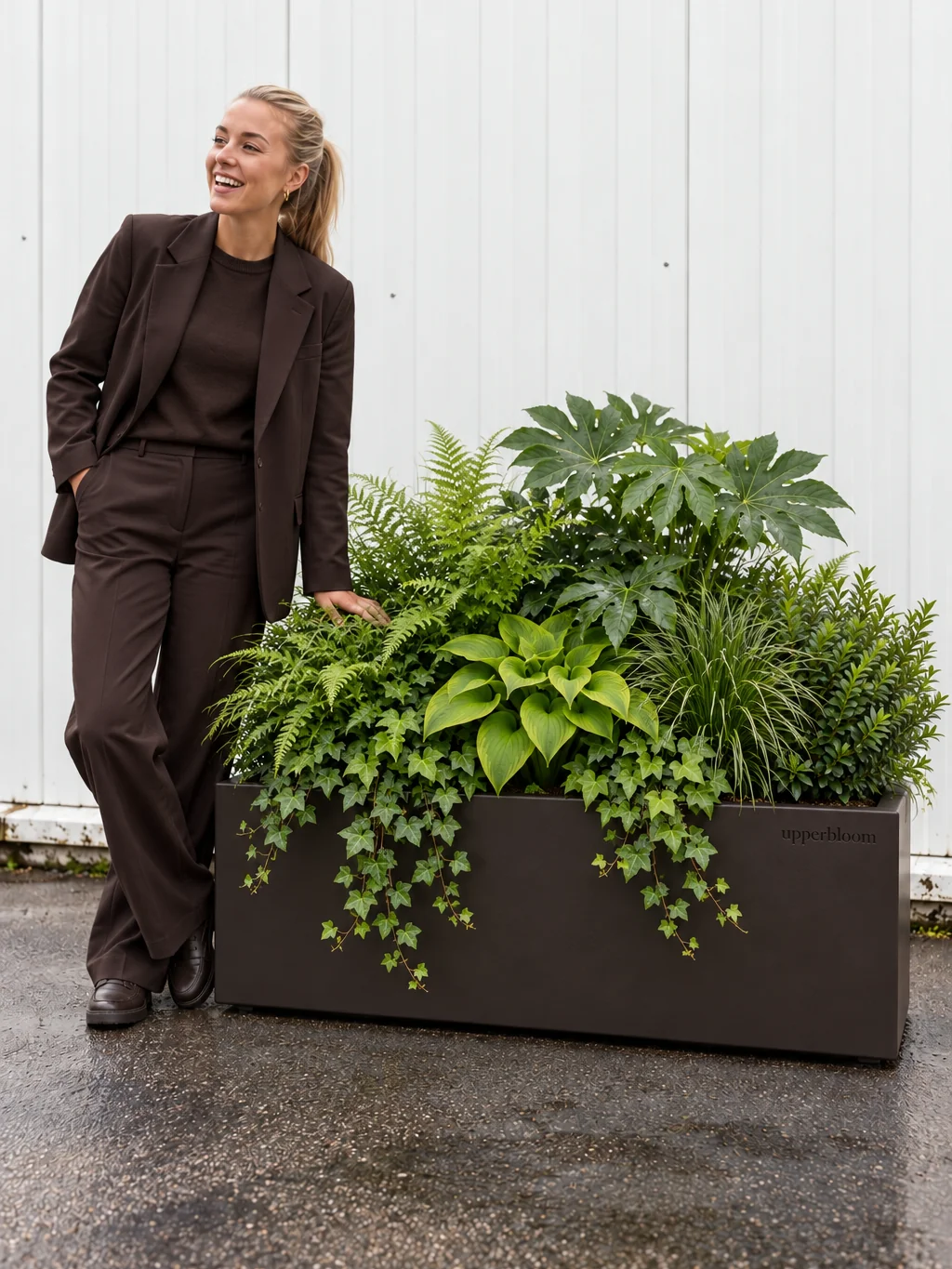 Vrouw naast een donkere rechthoekige plantenbak met varens, hosta en hangende klimop