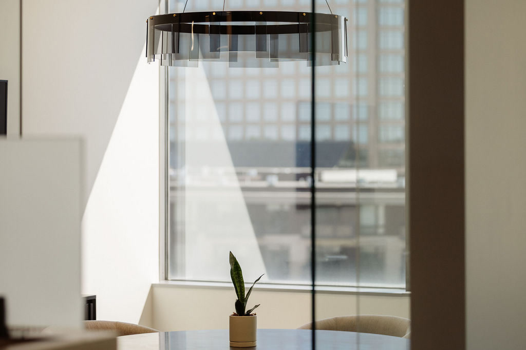 Meeting room with a round table and ring pendant light, seen through a glass wall