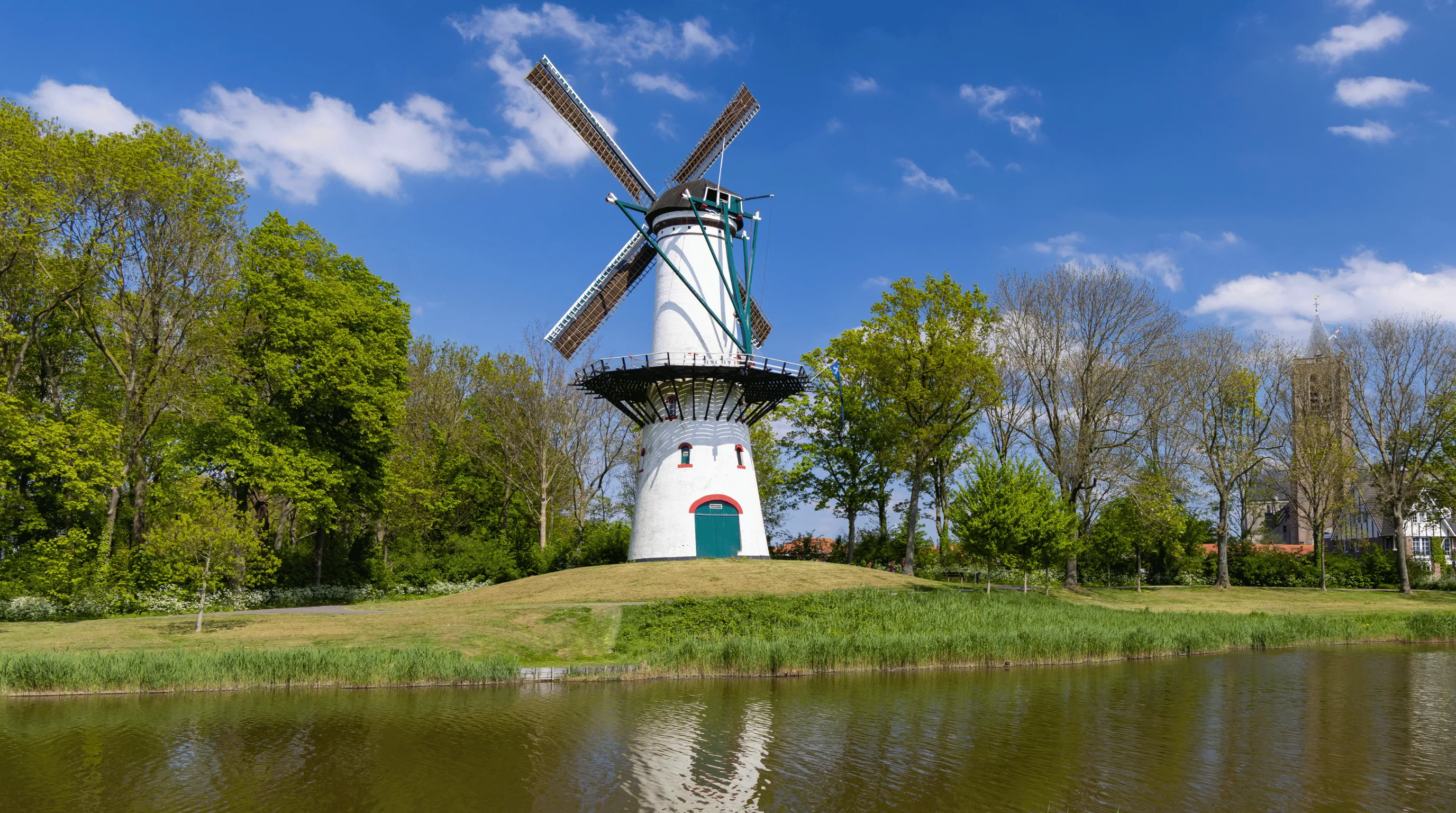 Traditionele Nederlandse windmolen bij het water in Tholen, met een kerktoren op de achtergrond