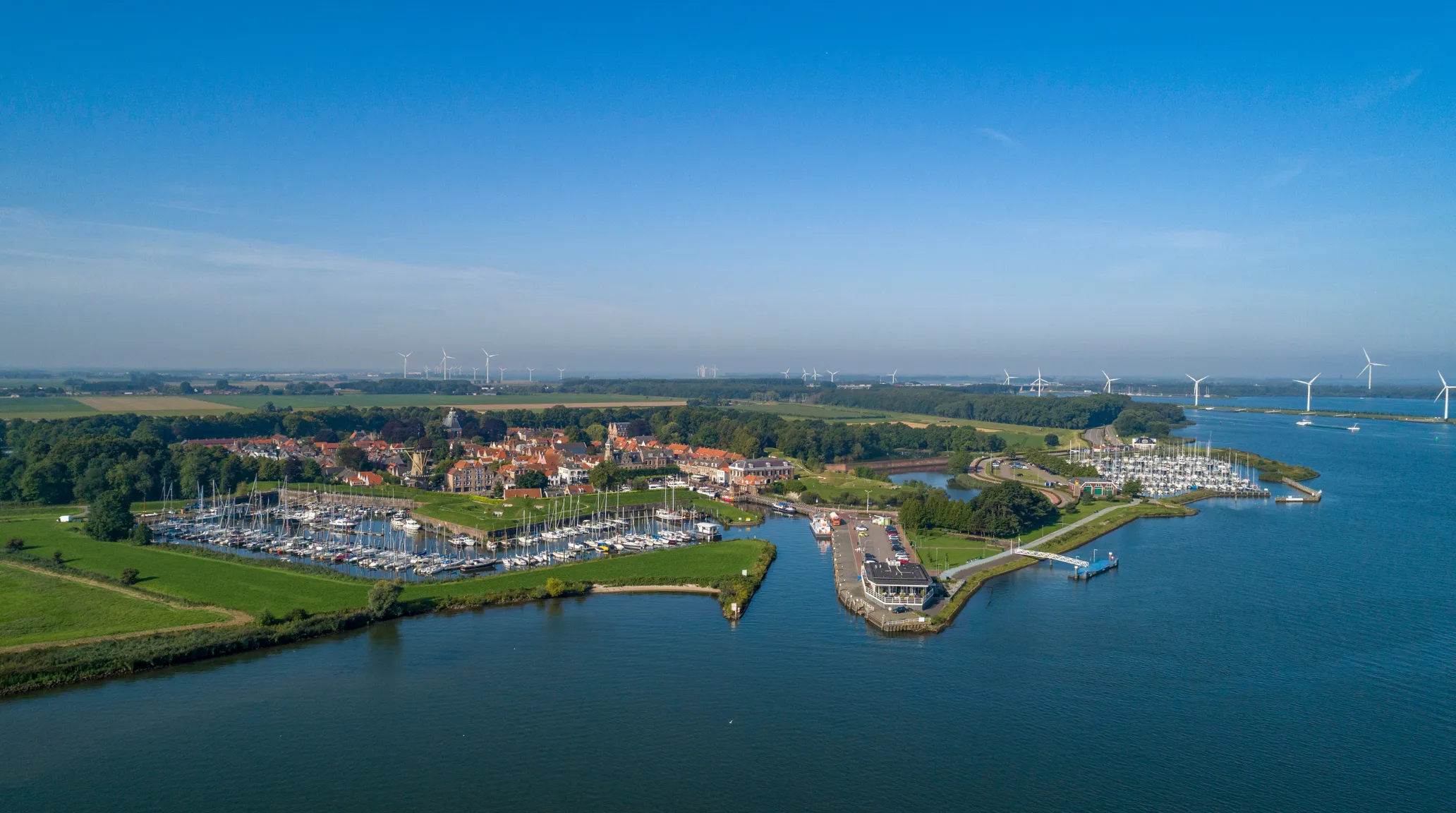 Luchtfoto van een havendorp aan het water in de gemeente Moerdijk, met jachthaven en windturbines aan de horizon