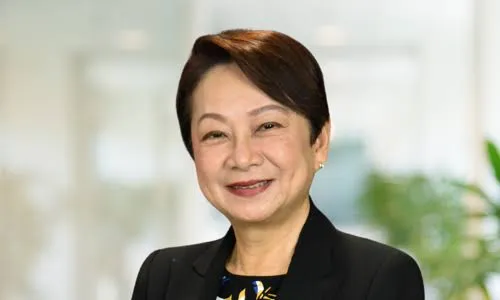 Smiling middle-aged woman with short dark hair wearing a black blazer and floral blouse.
