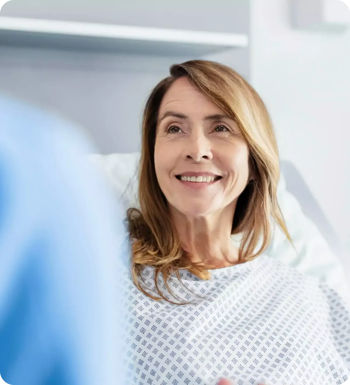 Smiling middle-aged woman in a hospital gown lying in a hospital bed.