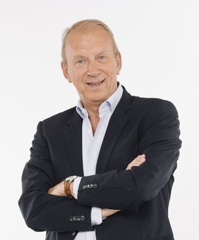 Smiling middle-aged man in a suit with arms crossed against white background.