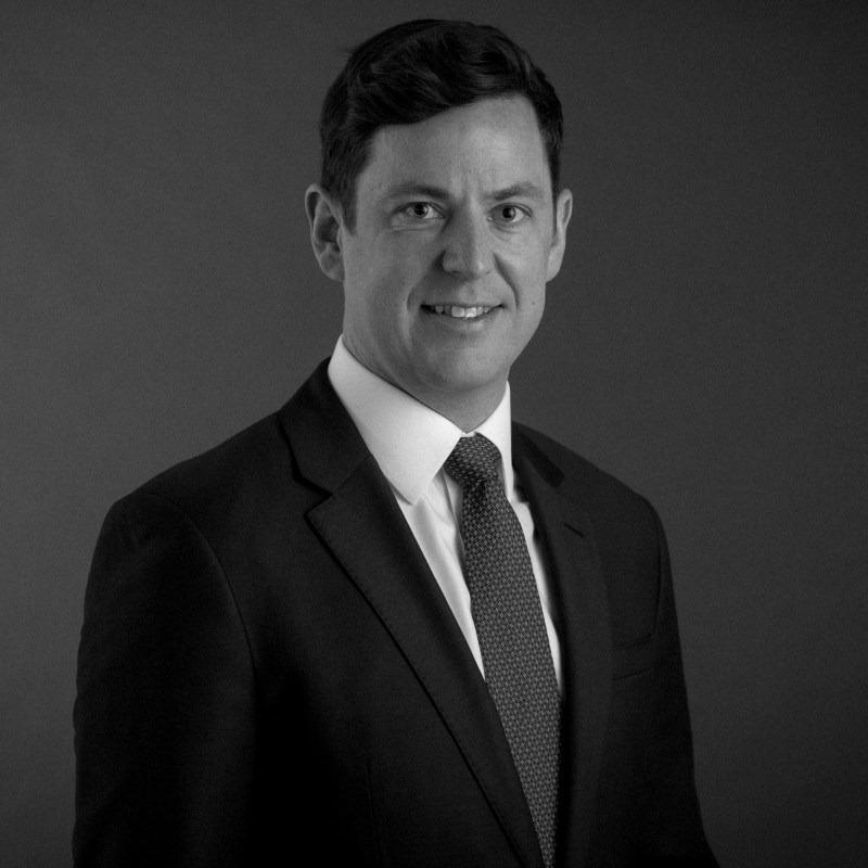 Man in a suit and tie posing against a plain dark background in black and white photo.