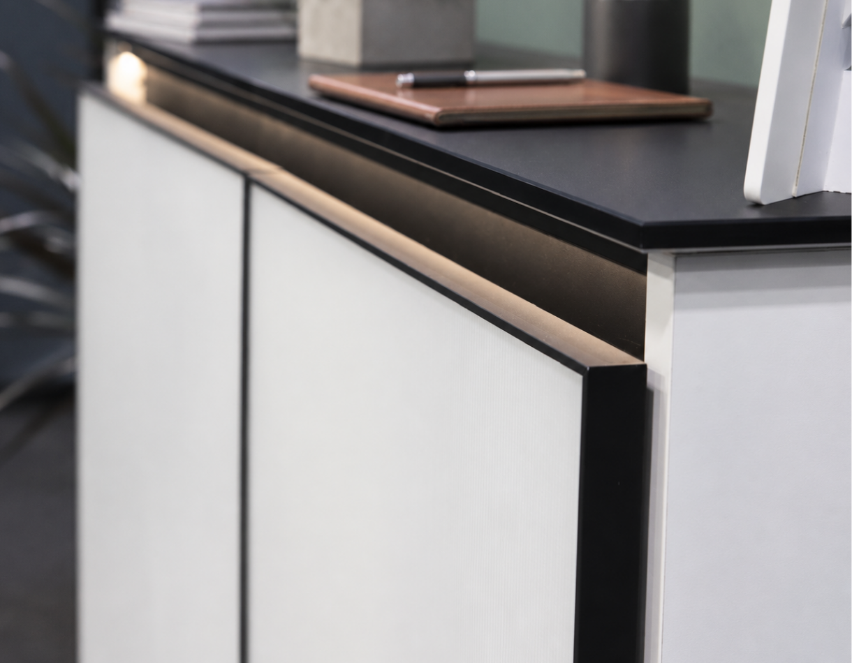 Modern showroom cabinetry featuring white backpainted glass cabinet doors, sleek black matte aluminum frames, integrated GOLA channels, and warm LED lighting