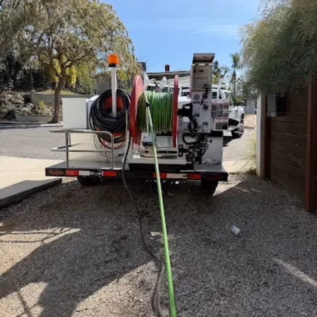Plumbing truck and drain cleaning machine set up outside a home for sewer maintenance.