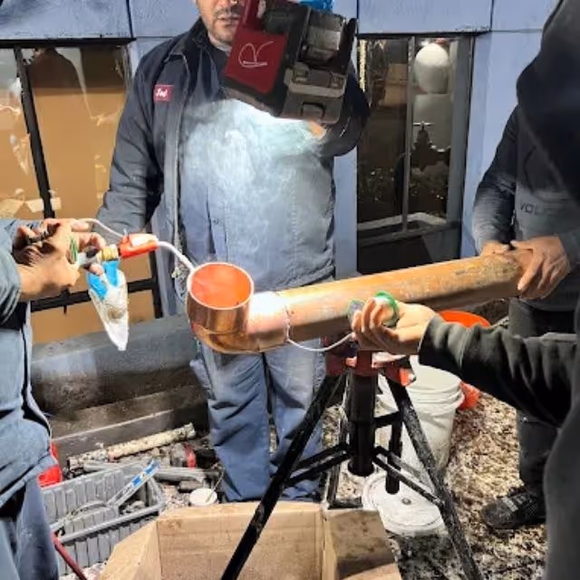 Plumbers soldering copper pipe fitting during professional plumbing installation.