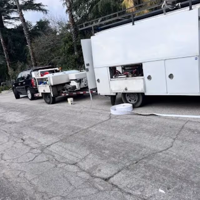 Plumbing service trucks parked on a residential street with equipment set up for sewer work.
