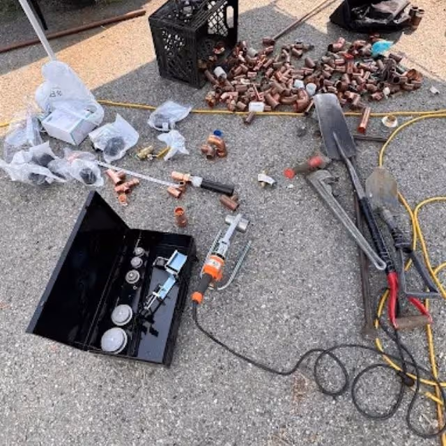 Plumbing tools and copper fittings beside open sewer cleanout for repair work.
