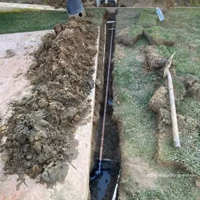 Excavated trench for underground sewer line replacement in residential yard.