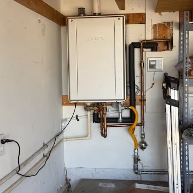 Tankless water heater installation with gas and water line connections in garage.