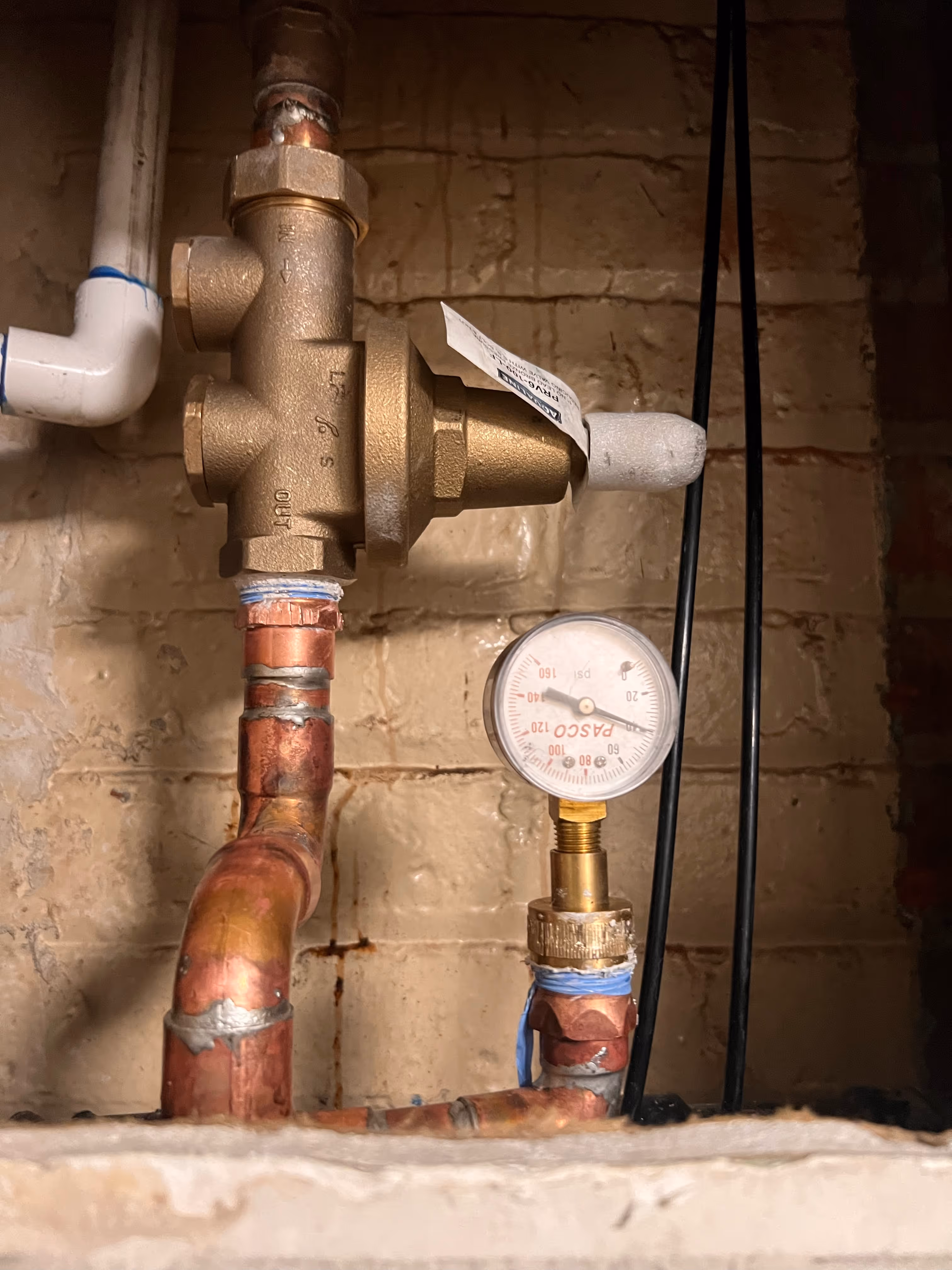 Water pressure regulator and gauge installed on copper plumbing line.