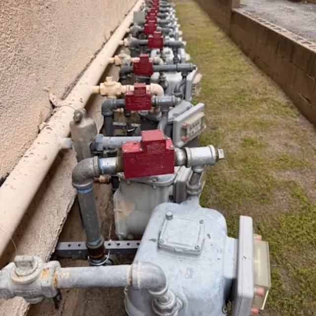 Row of residential gas meters and shut-off valves installed along exterior wall.