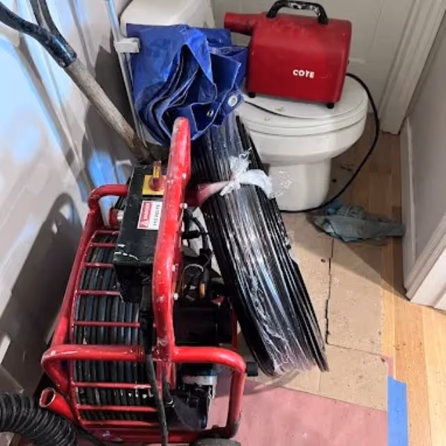 Drain cleaning machine positioned next to toilet for bathroom sewer service.