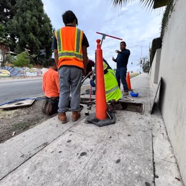 Plumbing crew performing sewer line repair at sidewalk access point.