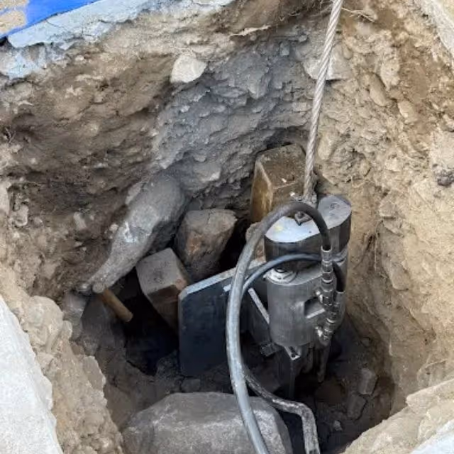 Hydraulic pipe bursting equipment positioned in excavation for sewer line replacement.