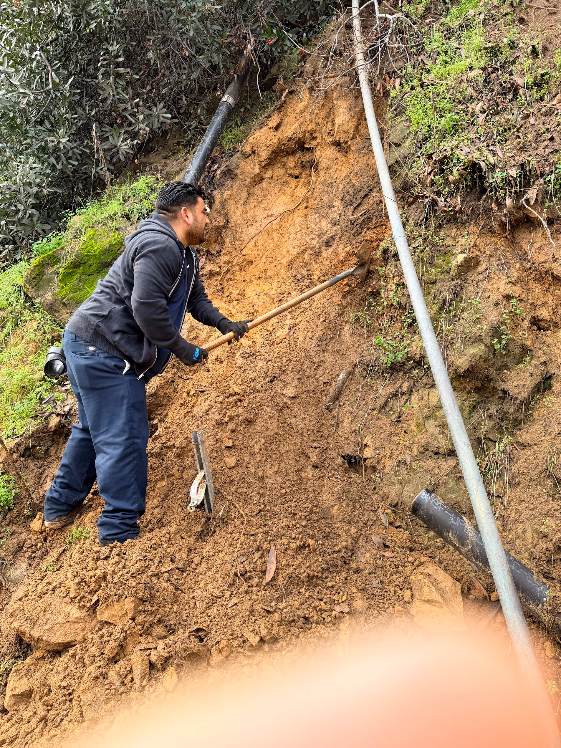 Trenchless sewer plumbing in Los Angeles, CA with a technician excavating soil to install pipe on a hillside.