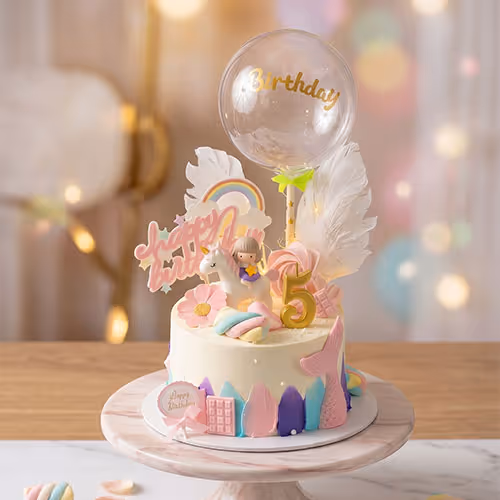White birthday cake with pastel decorations, a unicorn figure, the number 5, and a clear balloon topper.