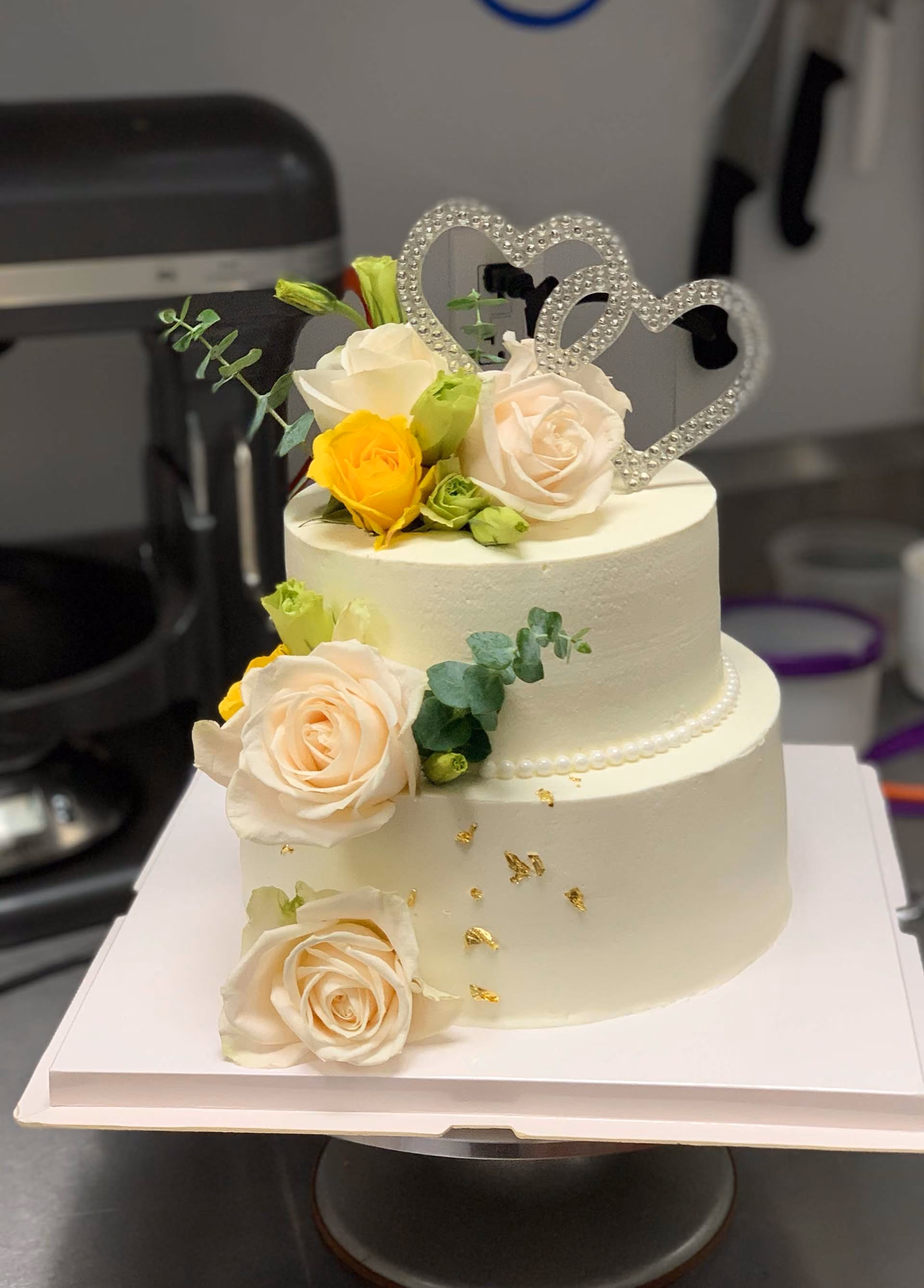 A white wedding cake with a gold heart on top.