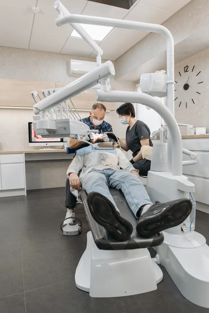 Dentist and dental assistant wearing masks treating a patient reclined in a dental chair in a modern clinic.