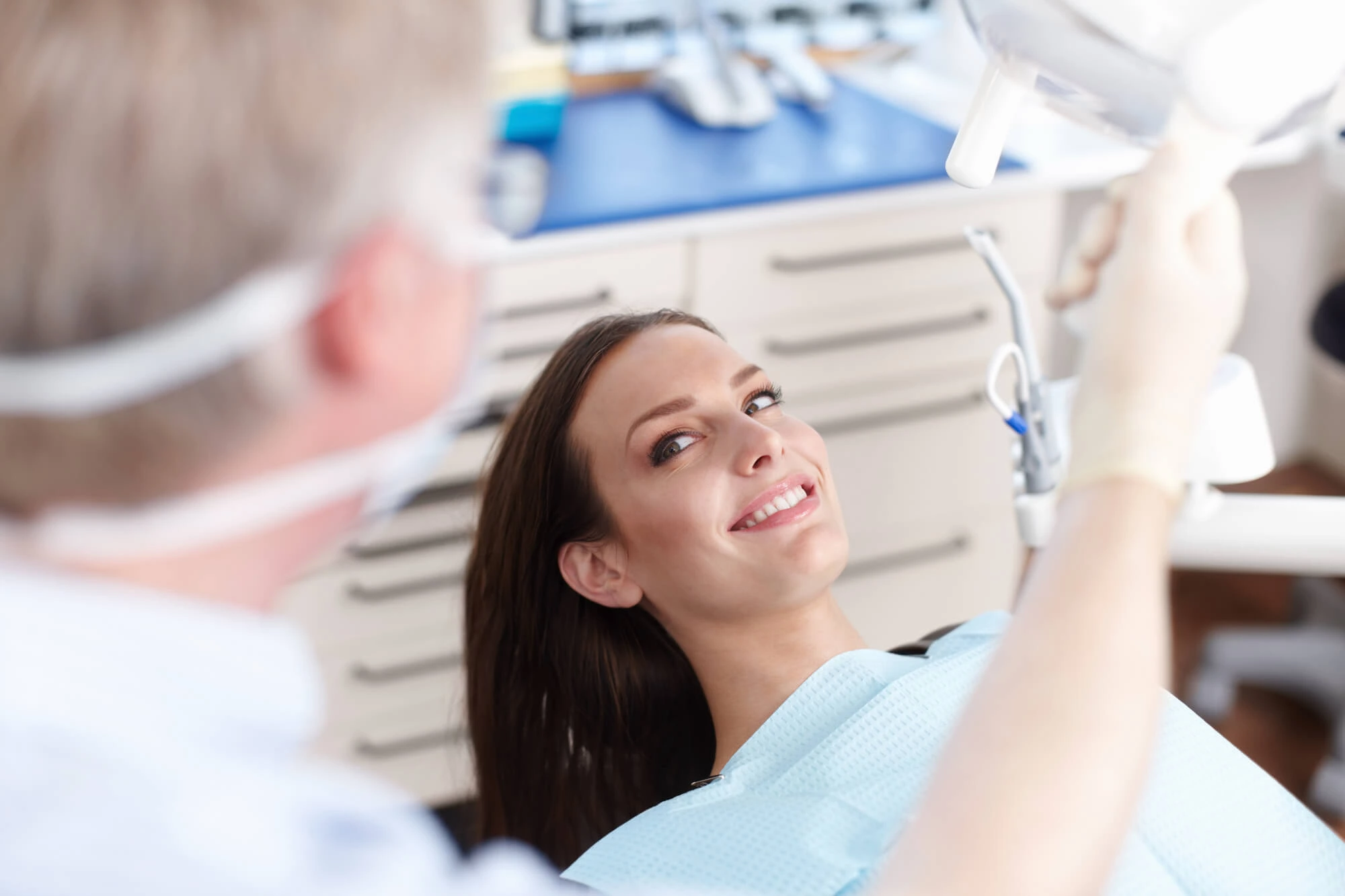 Smiling woman in dental chair looking at a dentist holding a dental light in a clinic.