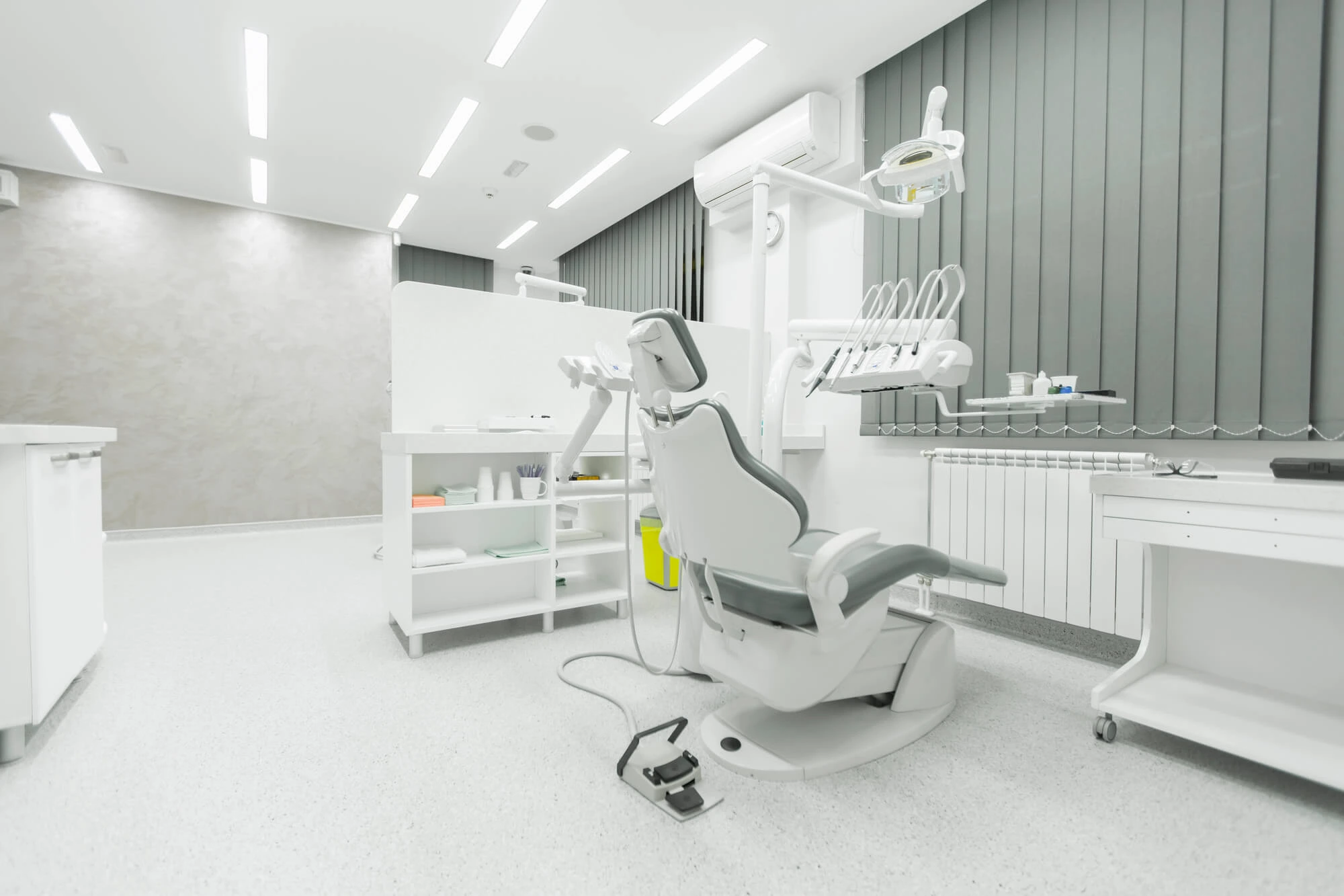 Modern dental clinic room with a white and gray dental chair and equipment.
