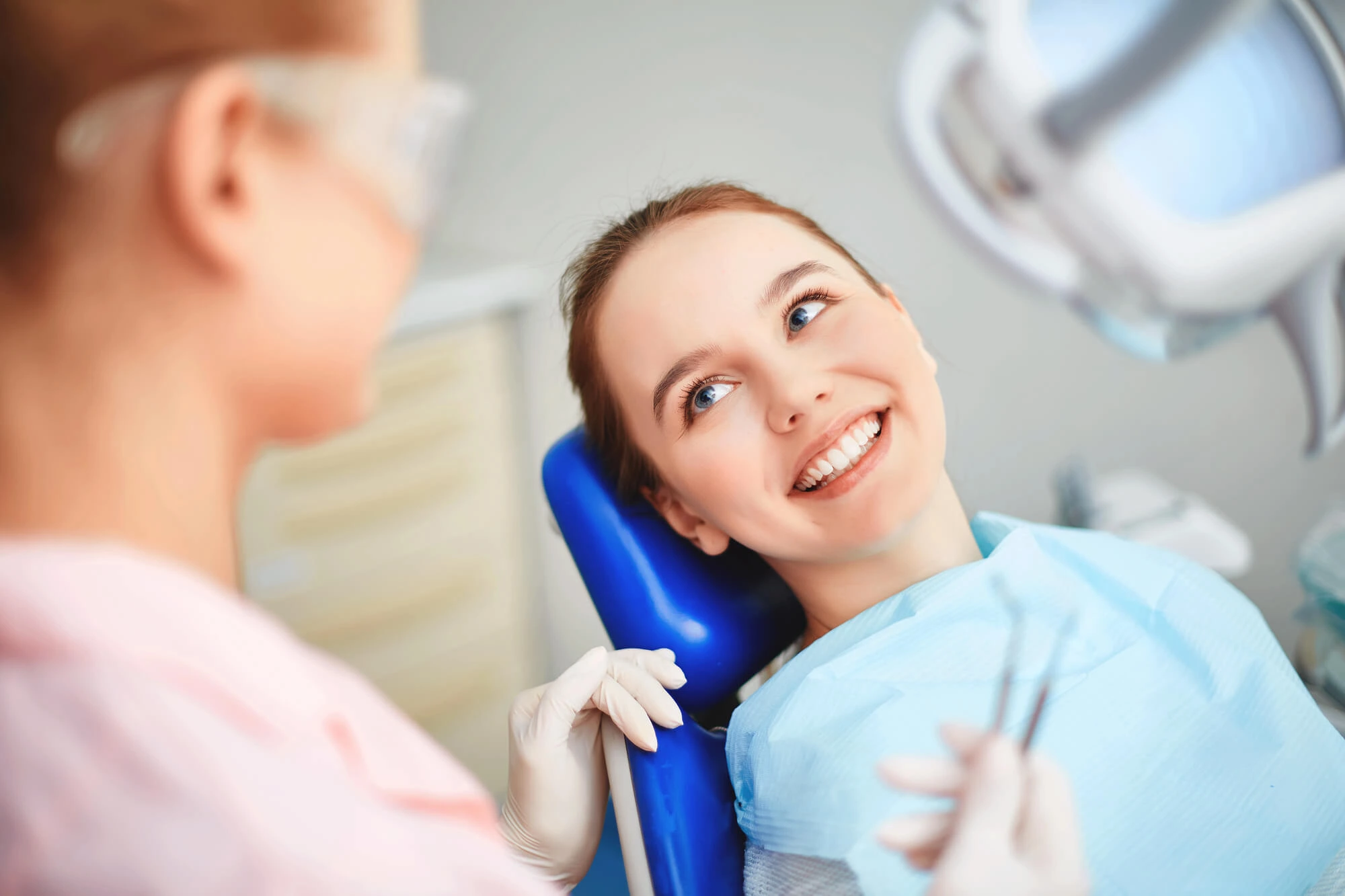 Smiling young woman sitting in a dental chair talking to a dentist.