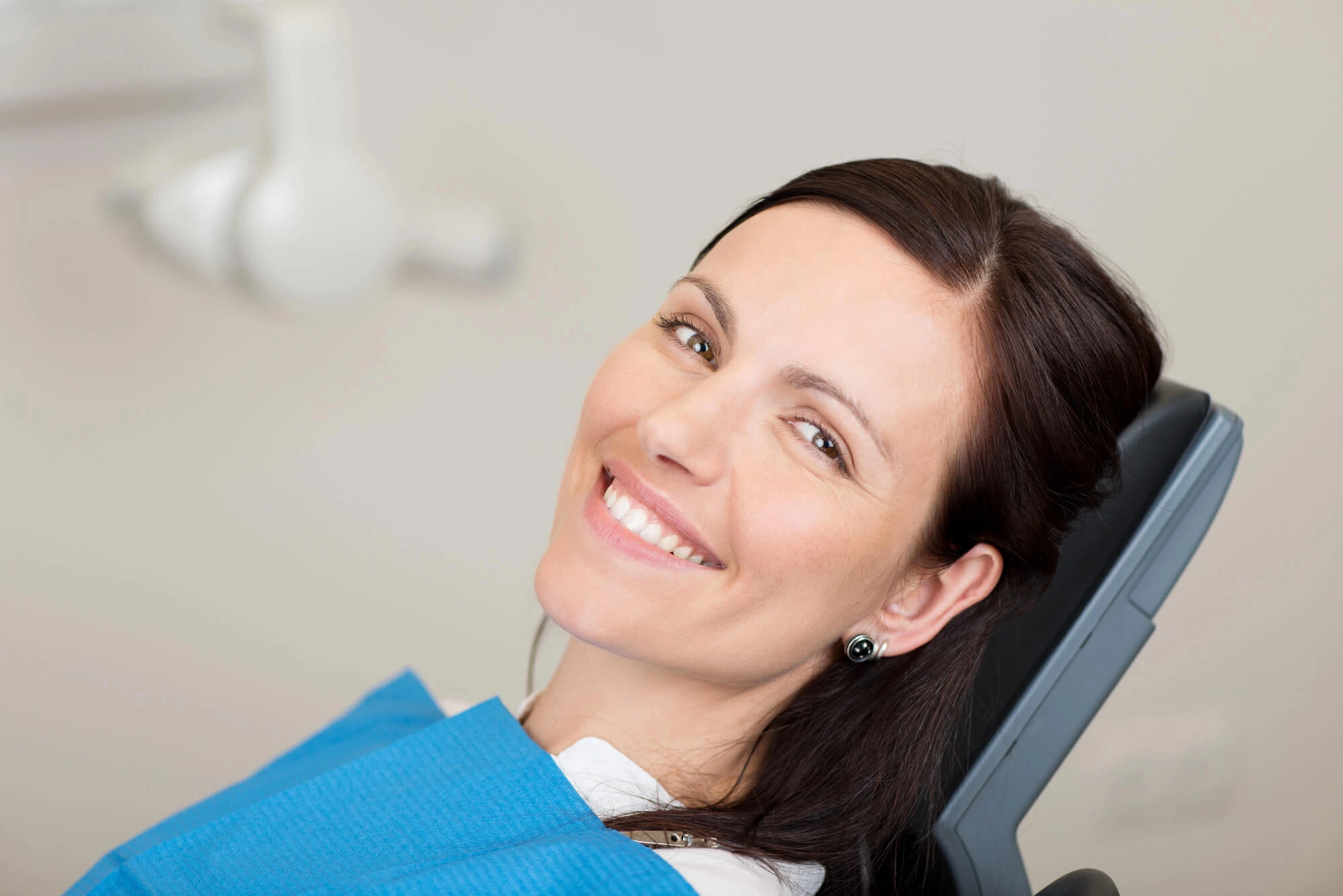 Smiling woman reclined in a dental chair wearing a blue dental bib.