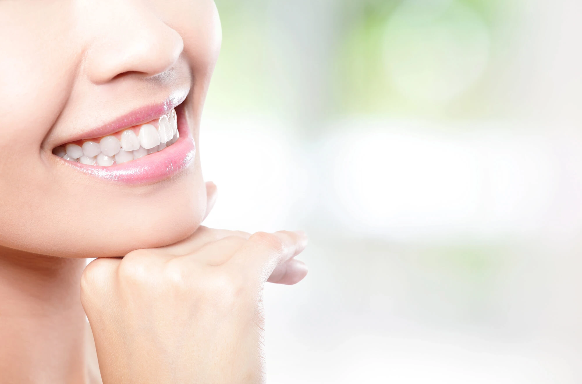 Close-up of a smiling woman resting her chin on her hand with white teeth and pink lips.