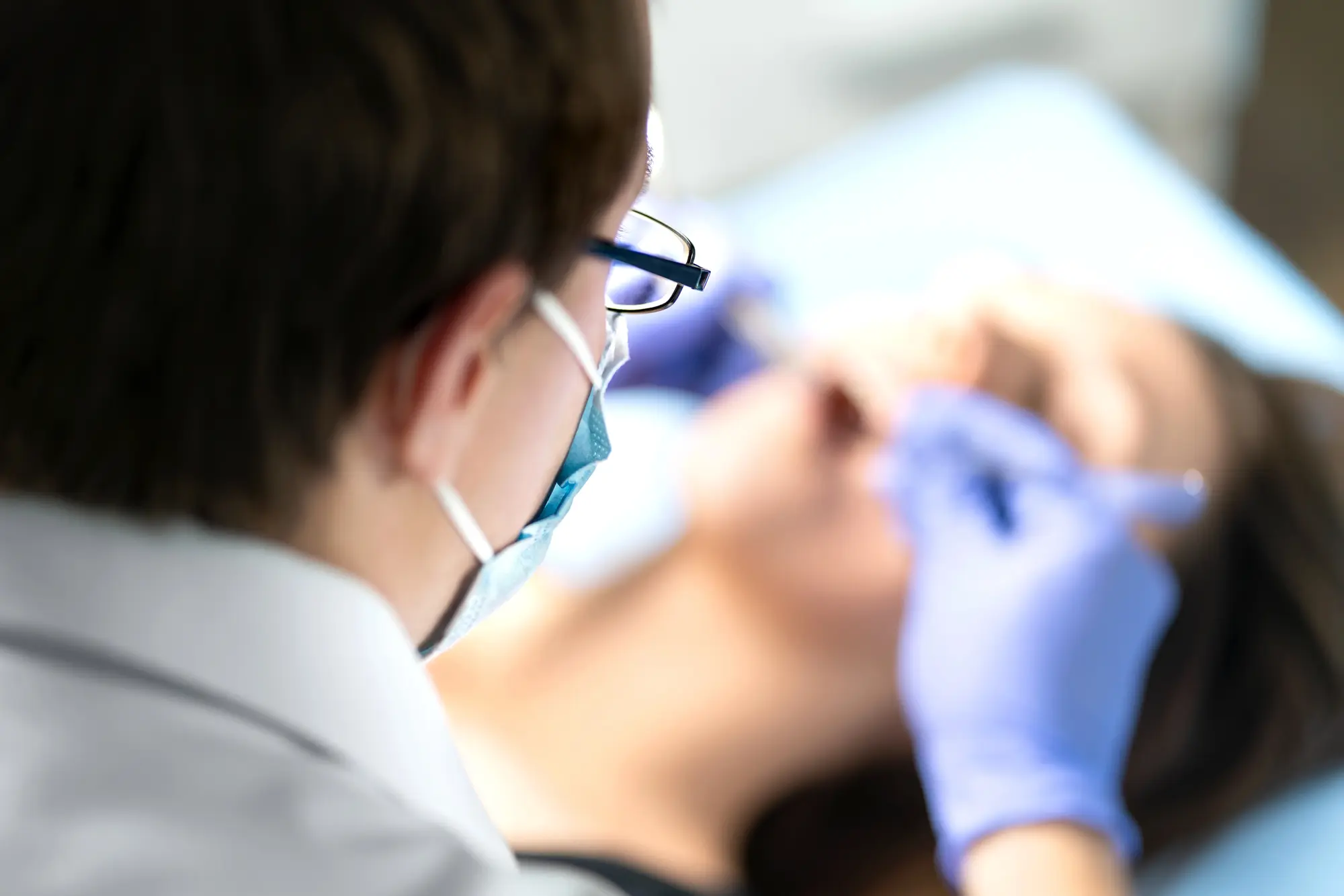 Medical professional wearing a mask and gloves treating a patient lying down.